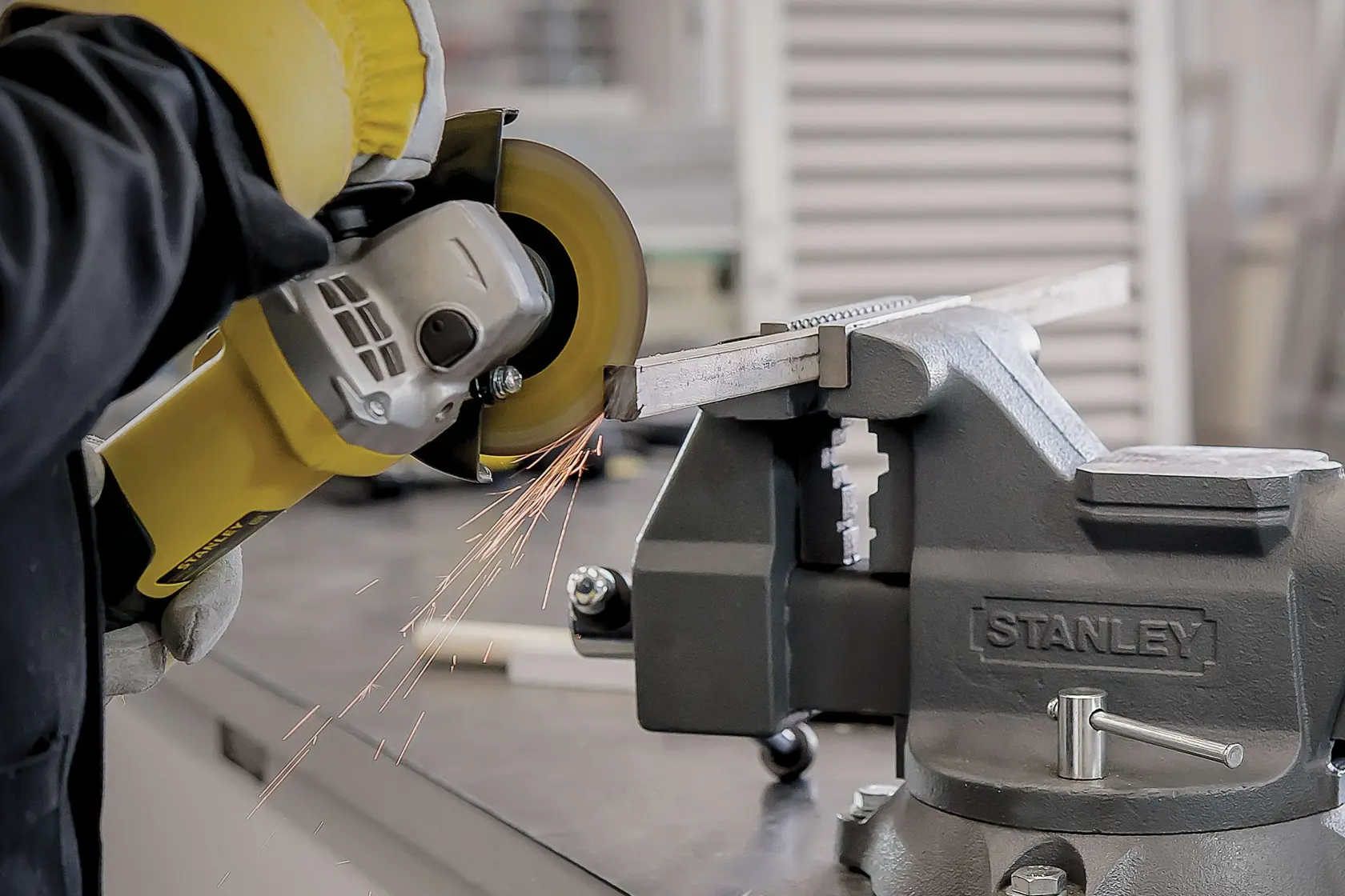Photo of STANLEY STA8061 bench vise holding metal bar, with angle grinder cutting and producing sparks.