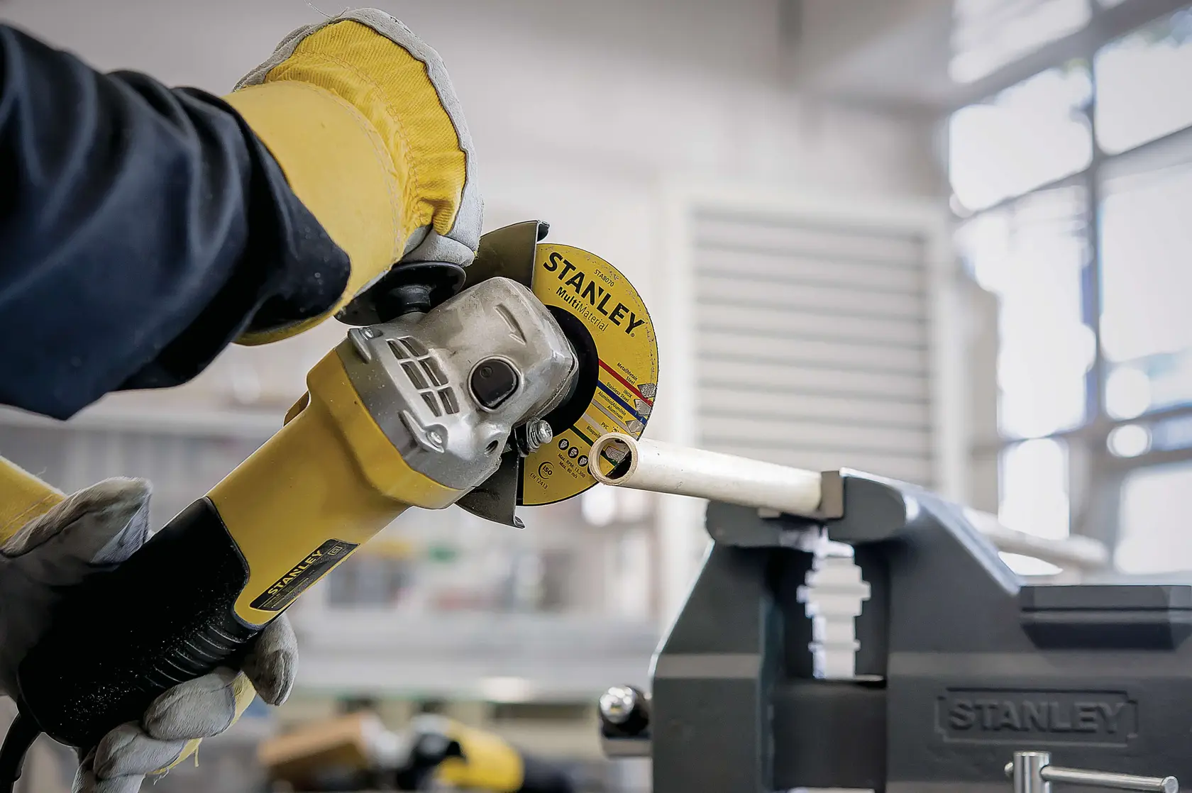 Photo of STANLEY STA8061 angle grinder cutting metal pipe in workshop, gloved hands holding tool.