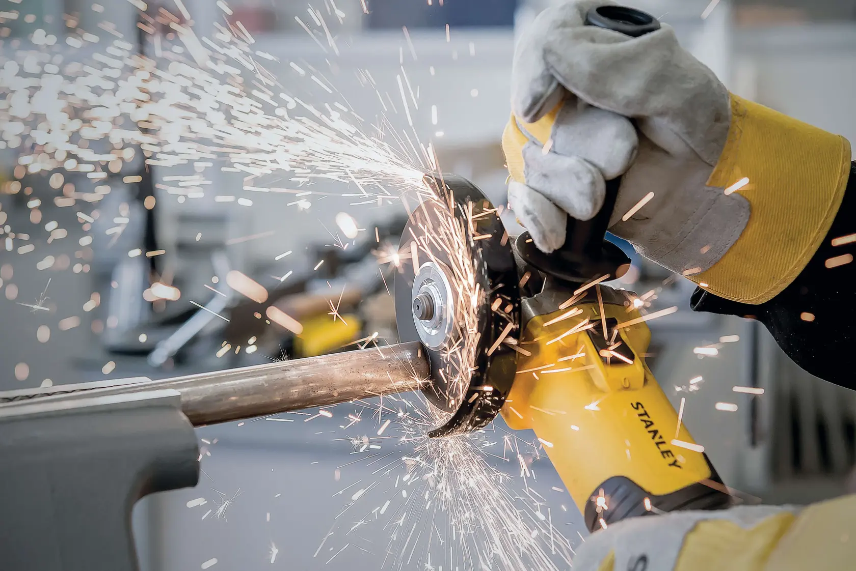 Photo of STANLEY STA8061 angle grinder in use, with sparks flying while cutting metal pipe, close-up action shot.