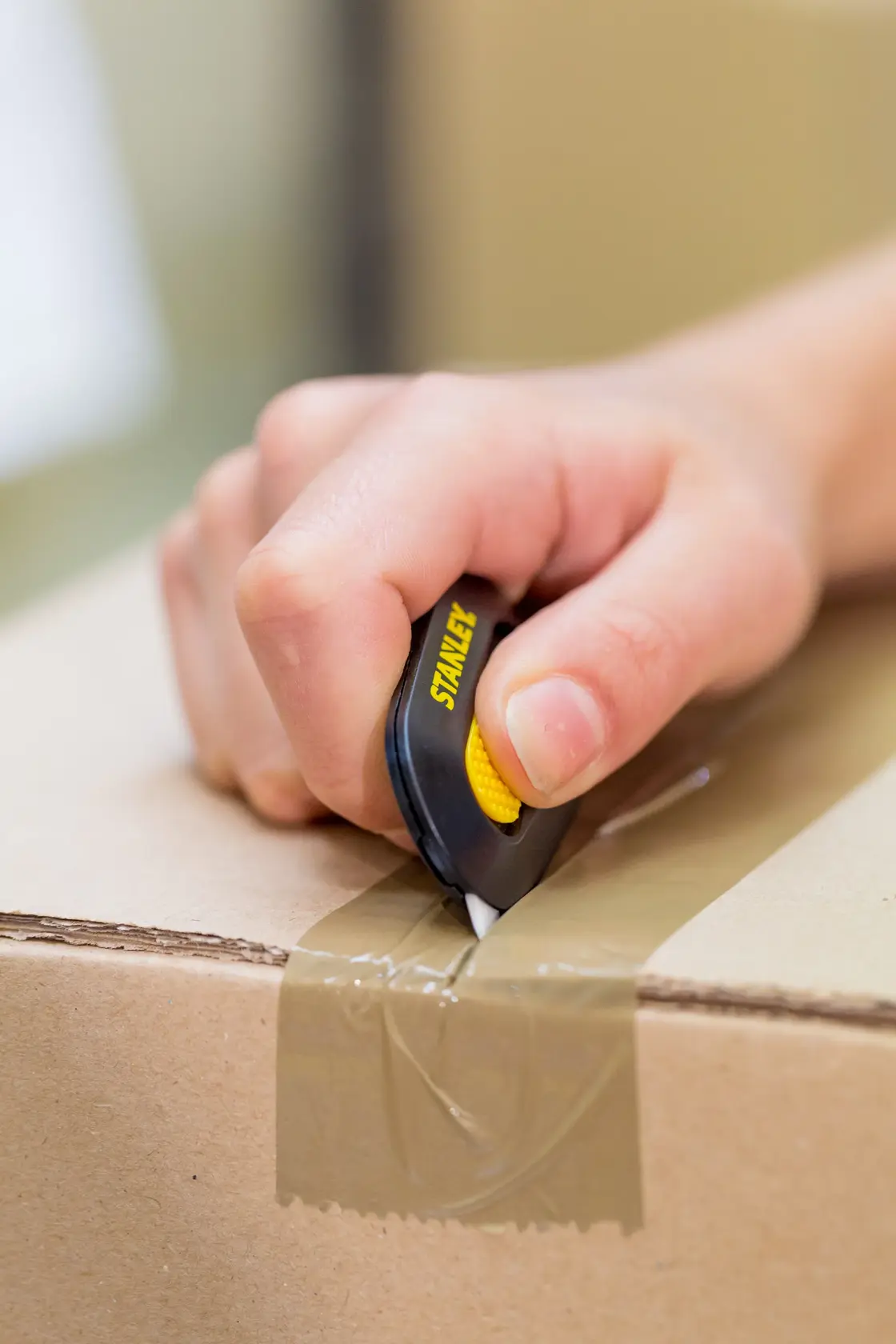 Photo of STANLEY STHT0-10292 utility knife cutting tape on cardboard box, handheld, product in use.