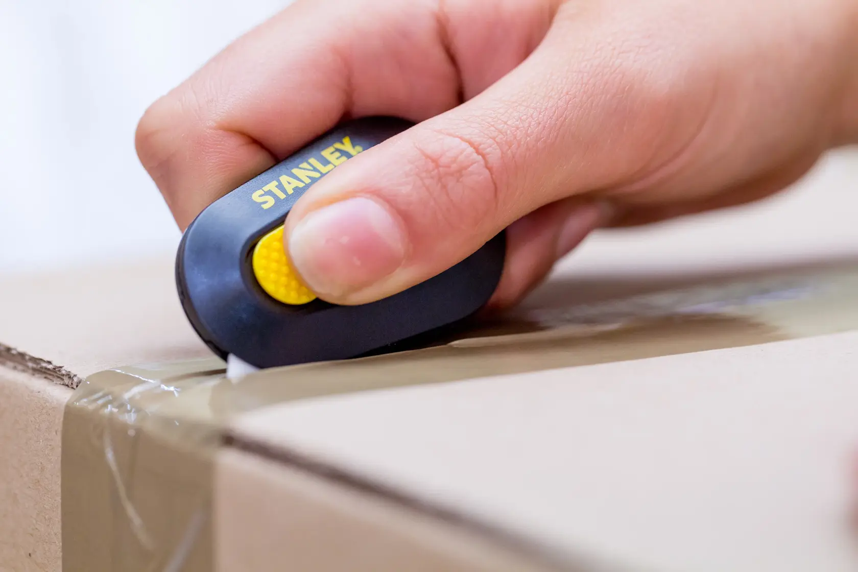 STANLEY STHT0-10292 compact box cutter in hand opening a taped cardboard box, close-up.
