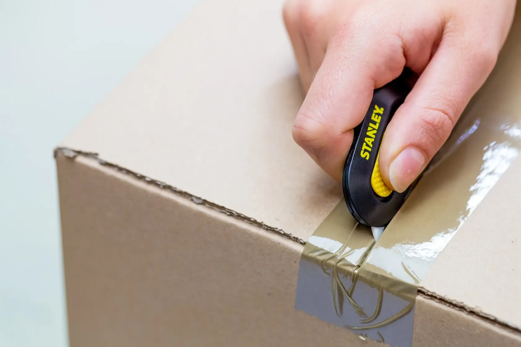 STANLEY STHT0-10292 utility knife cutting tape on a cardboard box, close-up view.