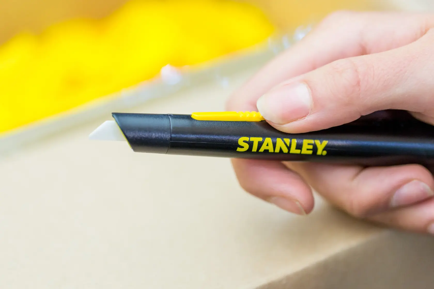 Photo of STANLEY STHT0-10293 utility knife with black handle and yellow slider, held in hand.