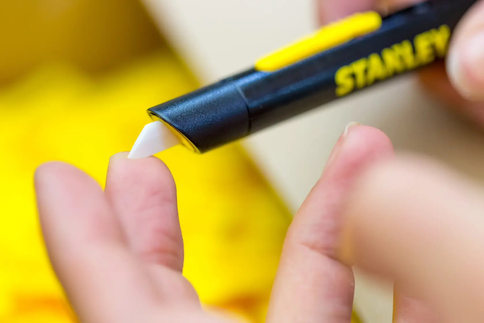 Photo of STANLEY STHT0-10293 safety knife with white blade used on a hand, close-up, product photography.