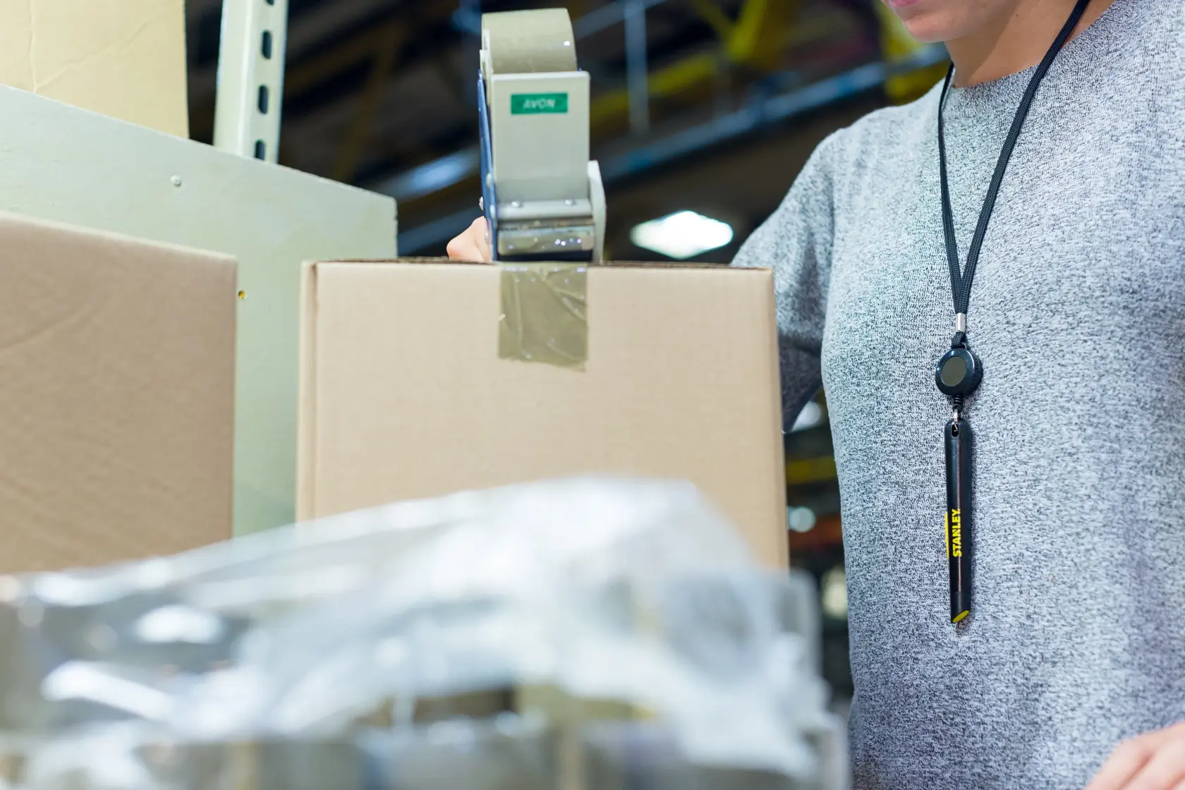 STANLEY STHT0-10293 utility knife hanging on lanyard worn by person packing cardboard box.
