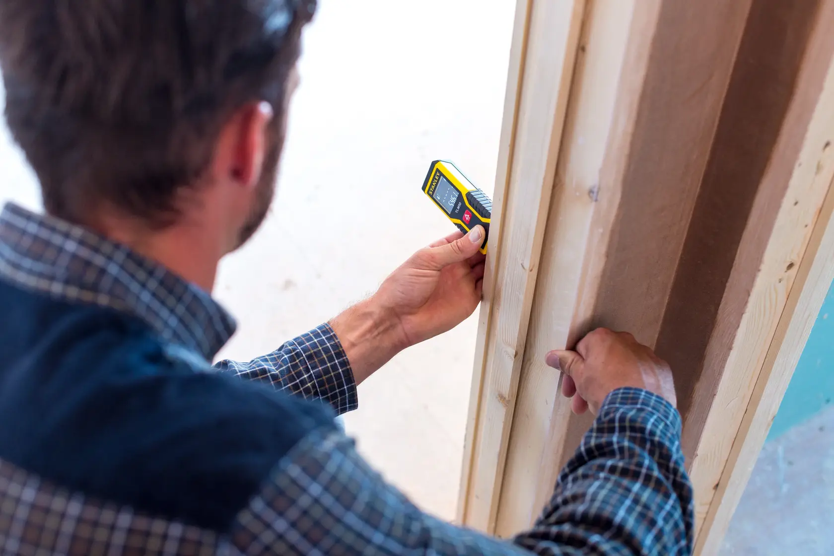Stanley STHT1-77409 digital laser distance measurer used by a person to measure a wooden door frame.