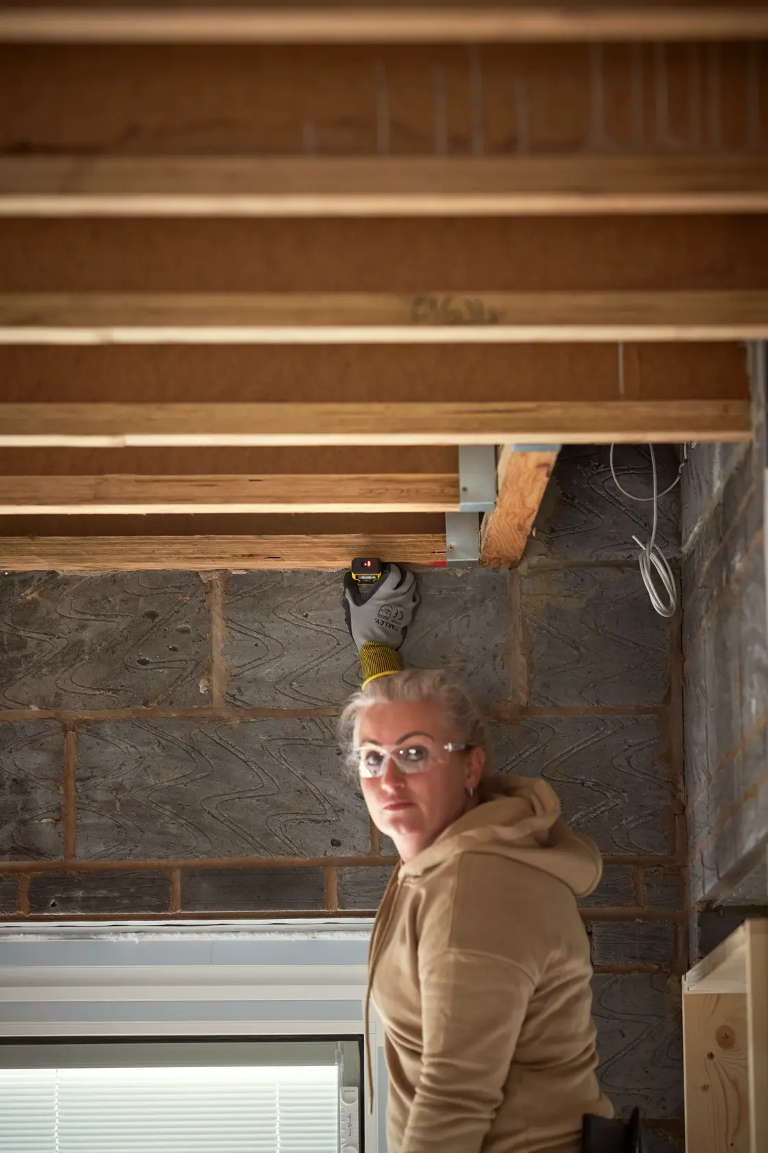 Photo of STANLEY STHT1-77409 laser distance measurer in use on exposed ceiling beams at construction site.