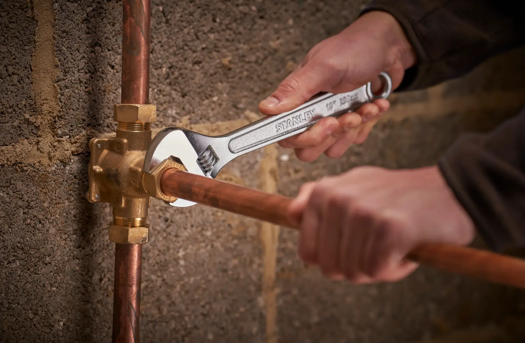 STANLEY STHT13156-0 adjustable wrench being used to tighten a copper pipe fitting against a masonry wall.