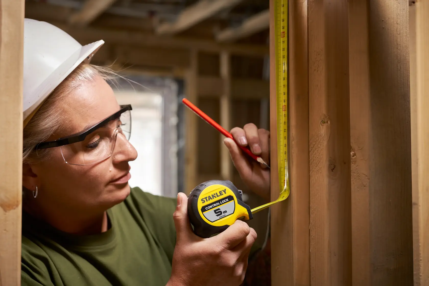 Photo of STANLEY STHT37231-0 tape measure in use, measuring wood framing, construction site background.