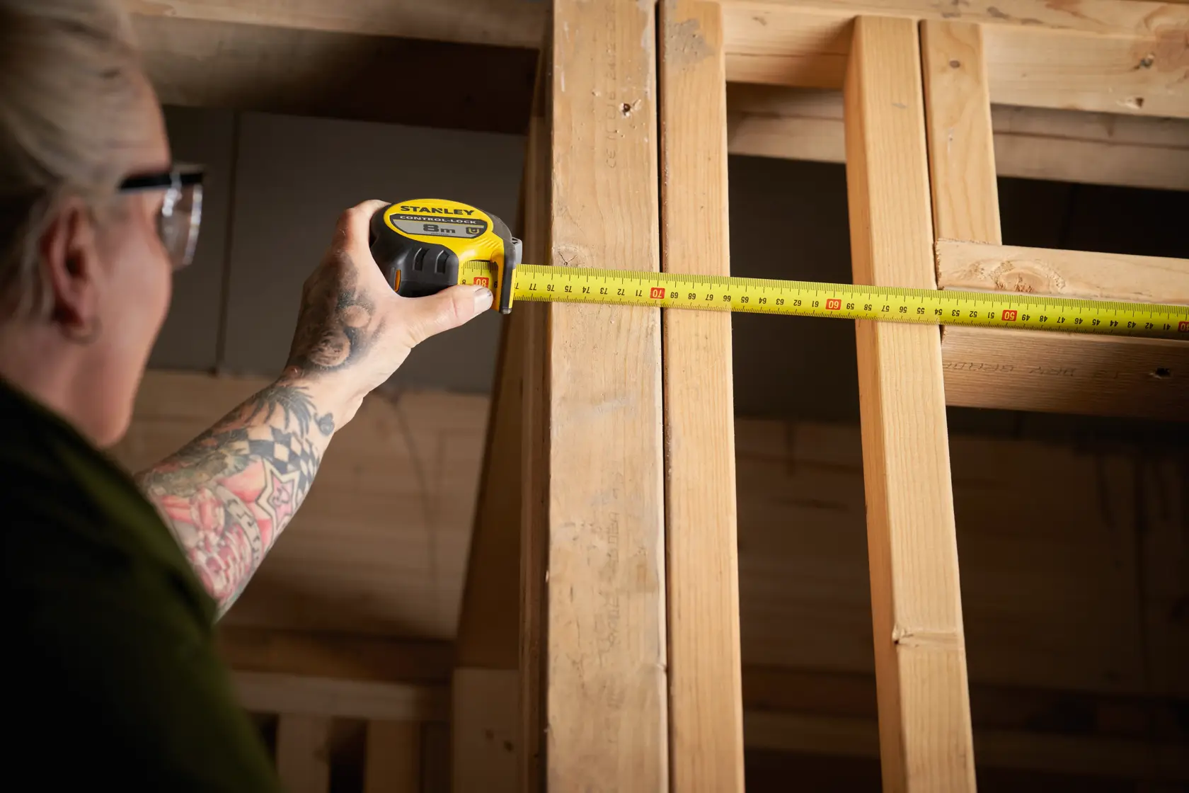 STANLEY STHT37232-0 tape measure in use measuring wooden beams, yellow and black tool, side angle.