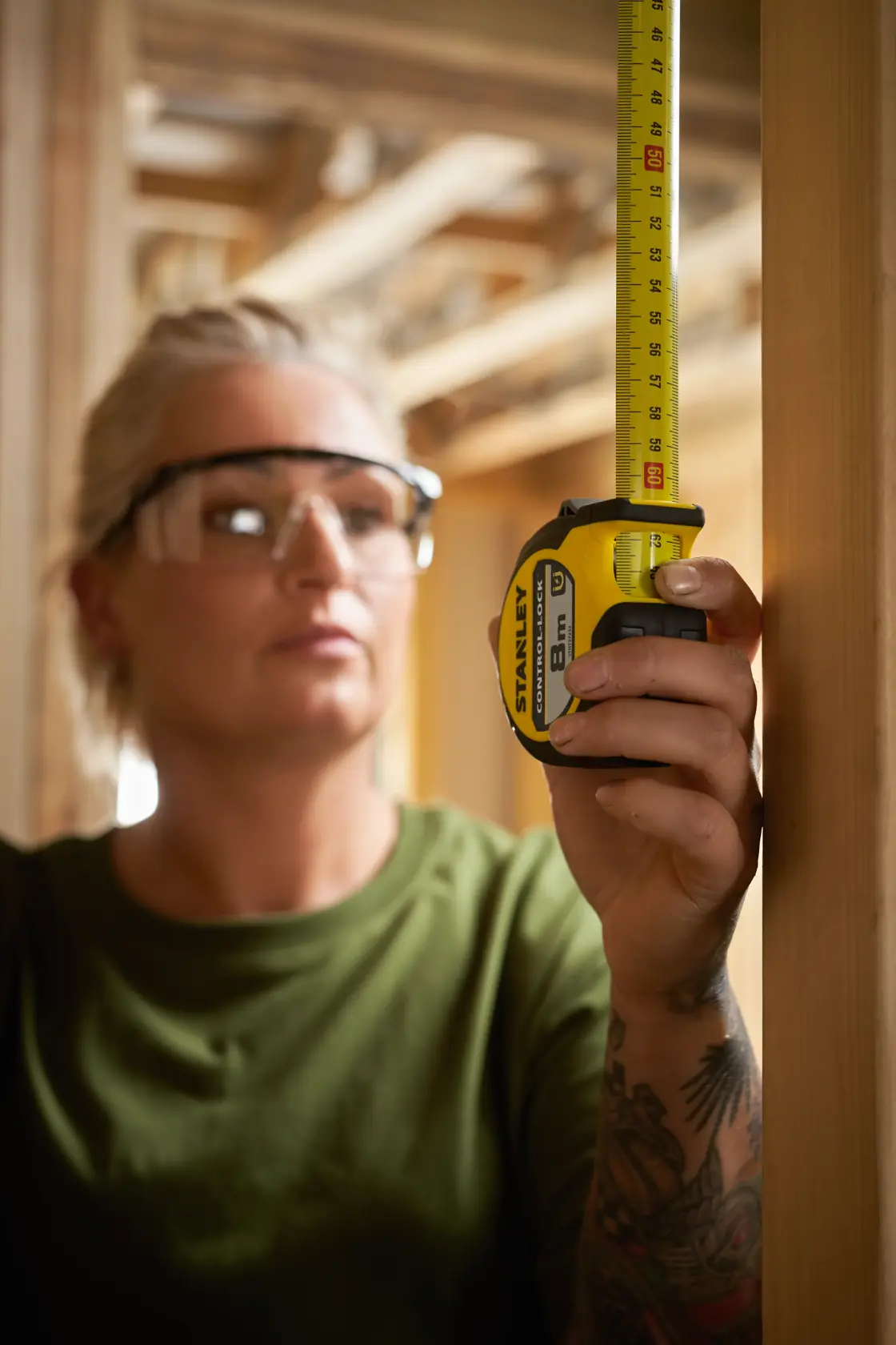 STANLEY STHT37232-0 tape measure held vertically against wood frame, focus on yellow and black tool.