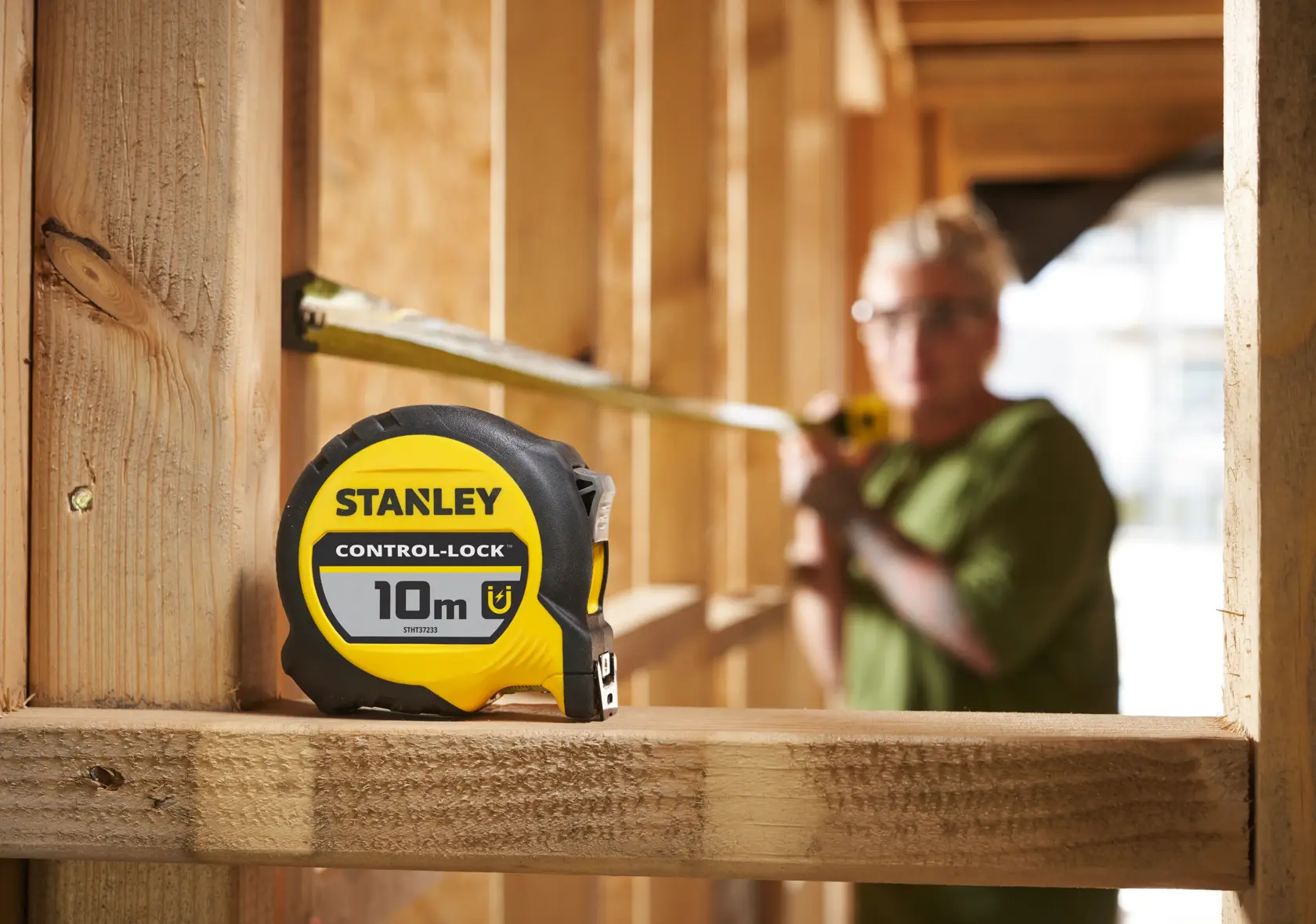 Stanley STHT37233-0 yellow and black tape measure, 10m, shown on a wooden construction site.