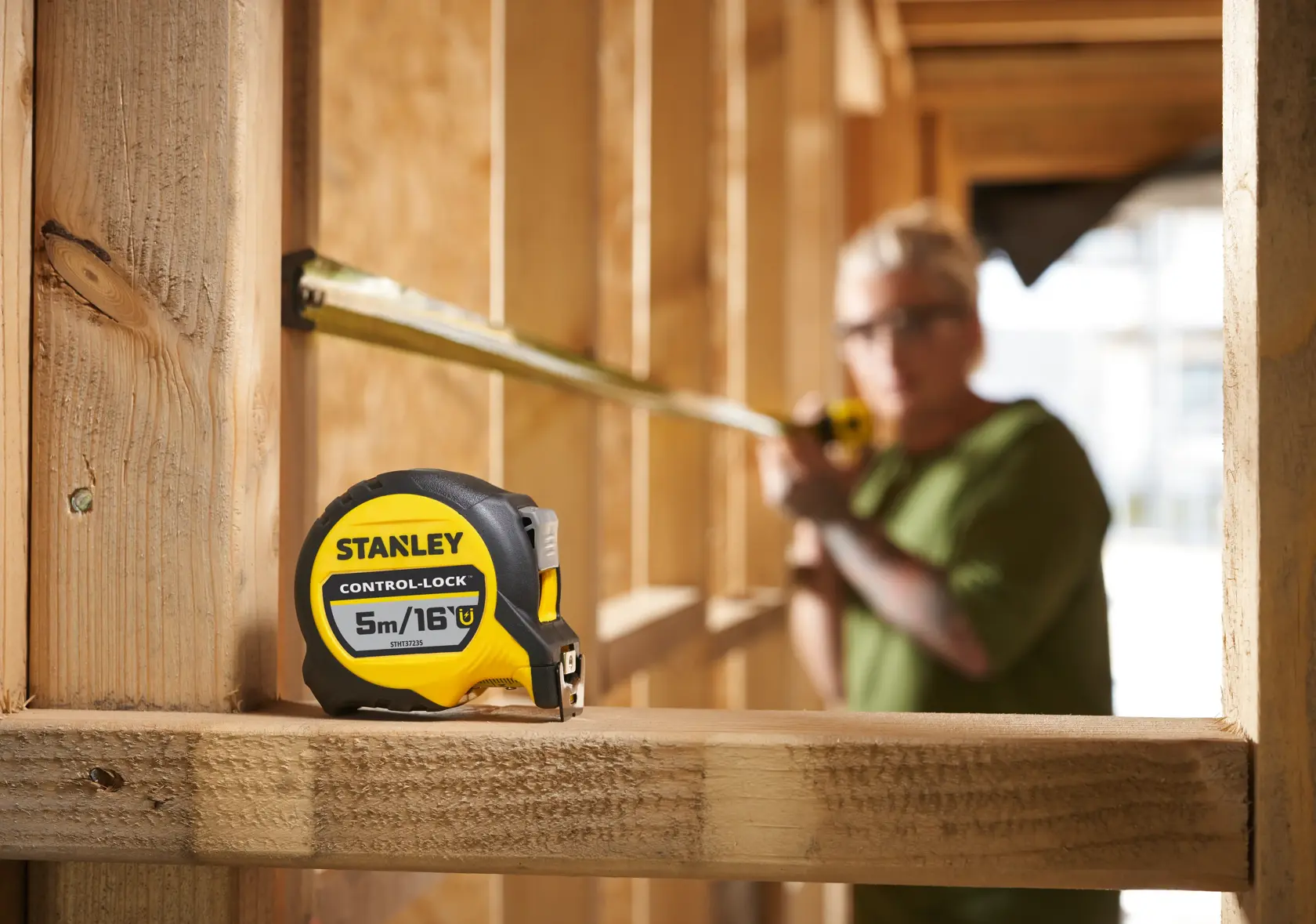 Stanley STHT37235-5 tape measure, yellow and black, on wooden beam at construction site, side view.