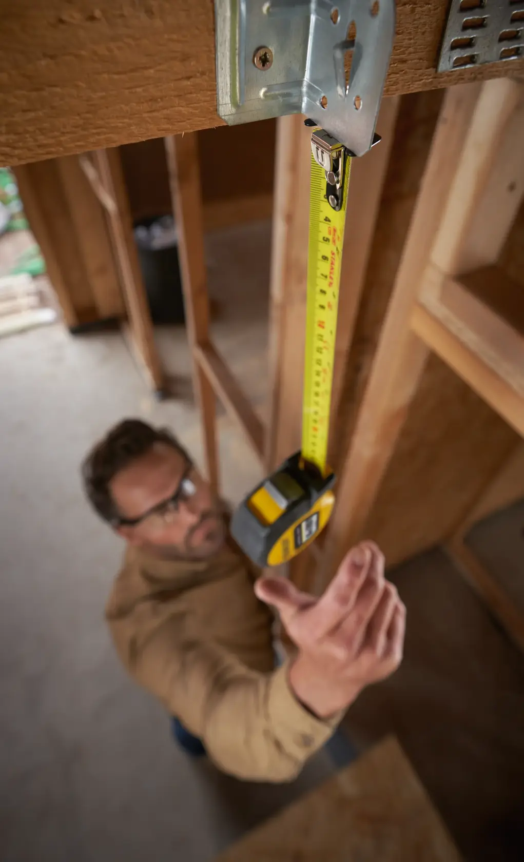STANLEY STHT37236-5 tape measure held vertically in construction site, yellow casing, handheld use.