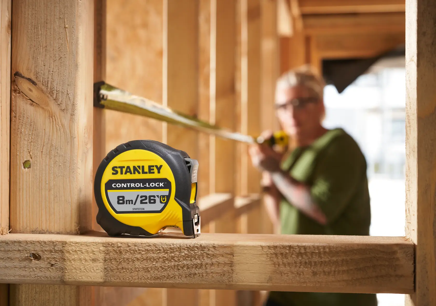 STANLEY STHT37236-5 tape measure on wooden beam, builder using tool, construction site background.