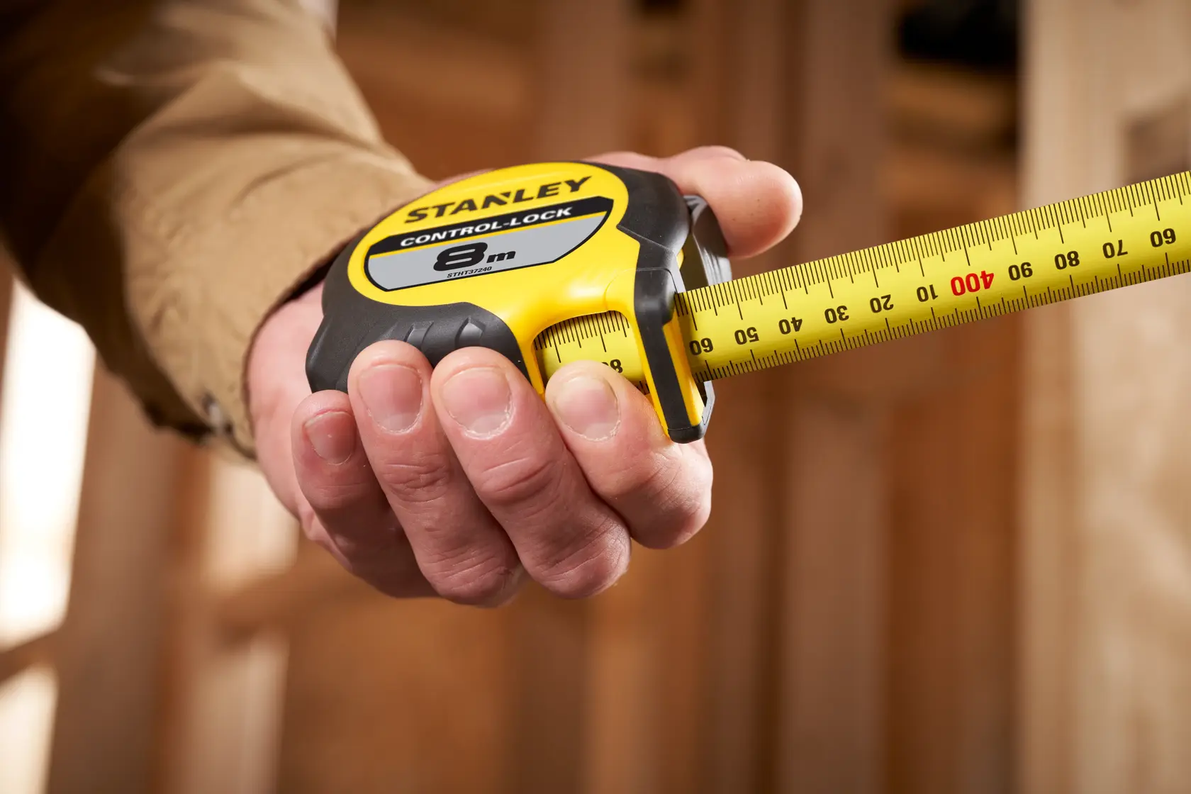 Photo of STANLEY STHT37240 tape measure, yellow and black, in a hand, with tape extended, indoor setting.