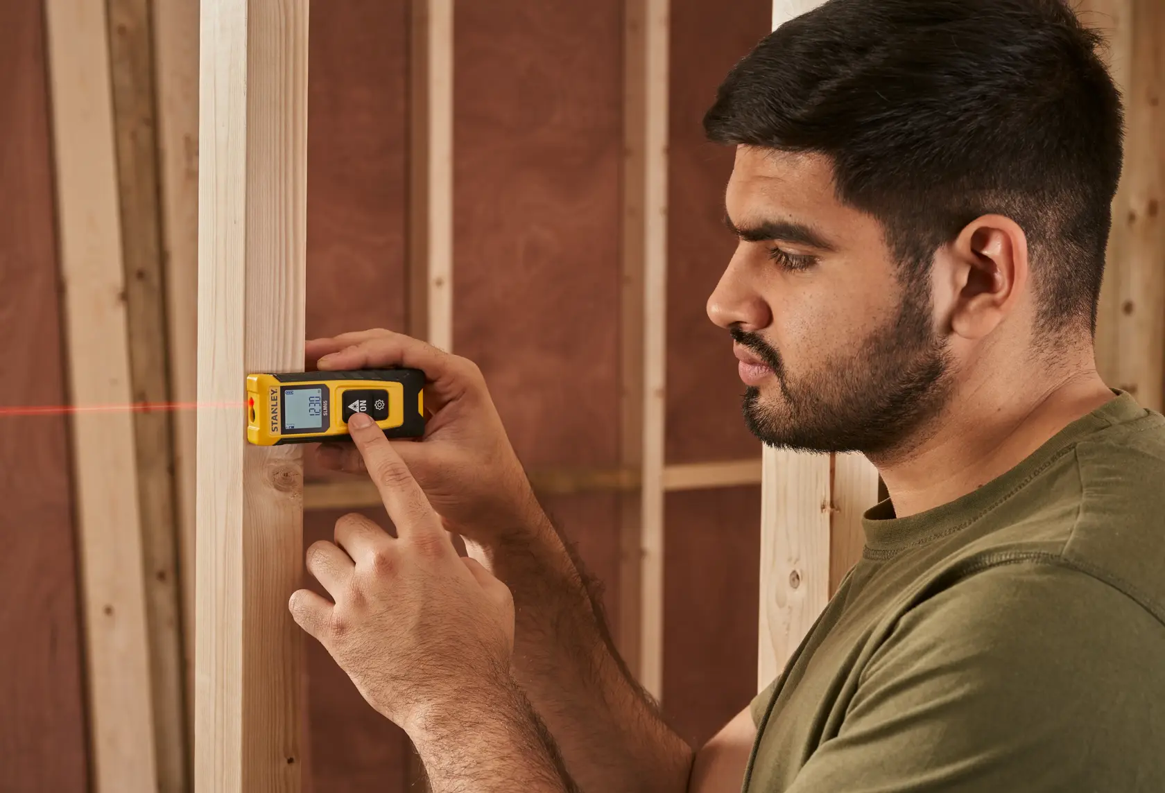 STANLEY STHT77065-0 laser distance measurer in use, showing display and red laser beam in construction setting.