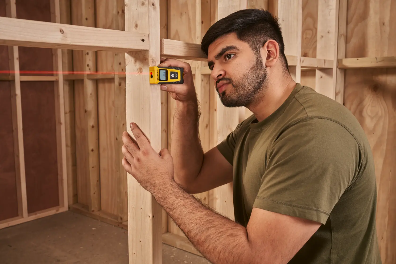 Photo of STANLEY STHT77065-0 laser distance measurer in use at a wood frame construction site.