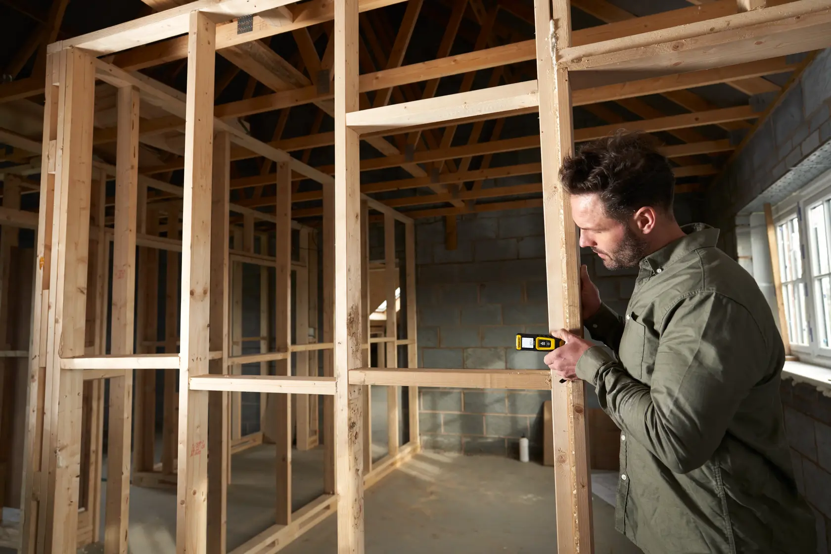 STANLEY STHT77100-0 laser distance measurer used on wooden frame in construction site, product in hand.