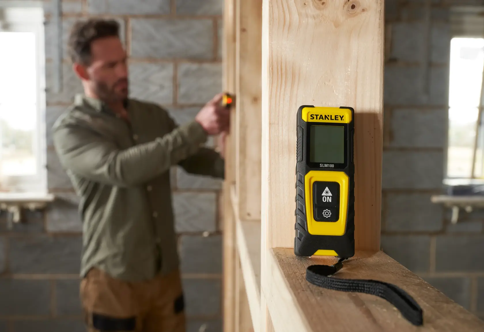 STANLEY STHT77100-0 laser distance measurer in black and yellow on wooden frame, construction scene.
