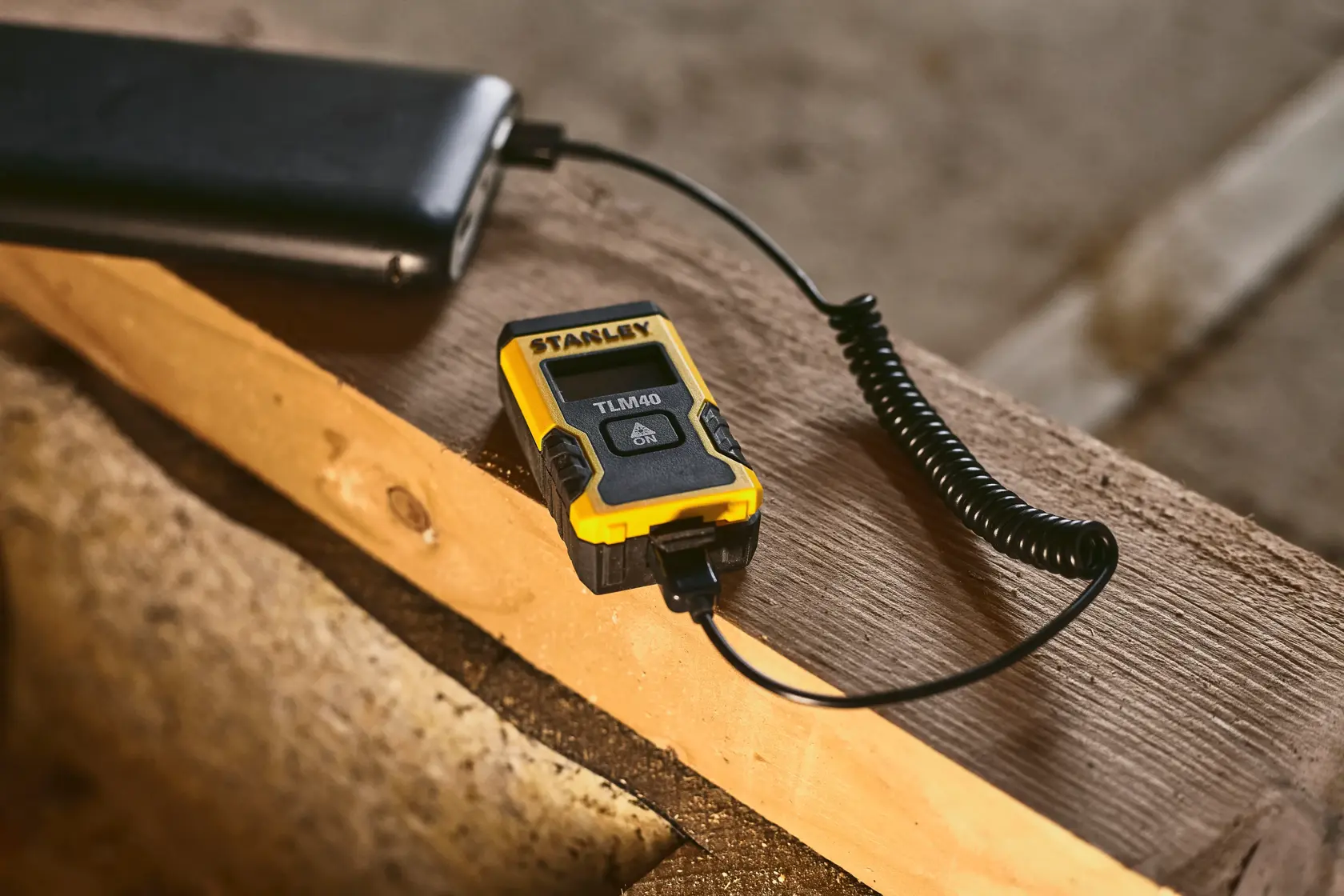 STANLEY STHT77666-0 laser distance measurer charging via USB cable on wooden surface.