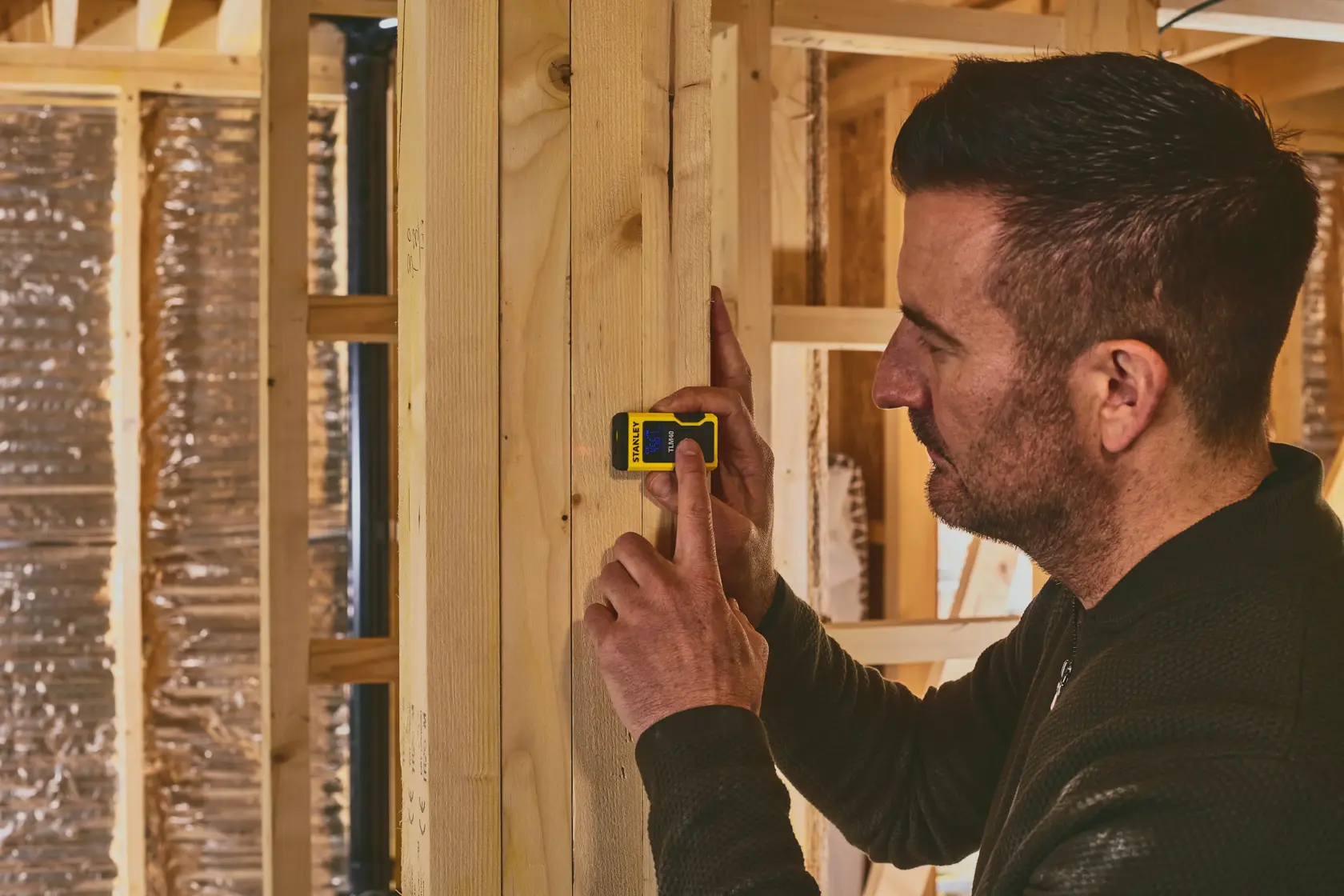 STANLEY STHT77666-0 laser distance measurer in use against wooden beam, interior construction setting.