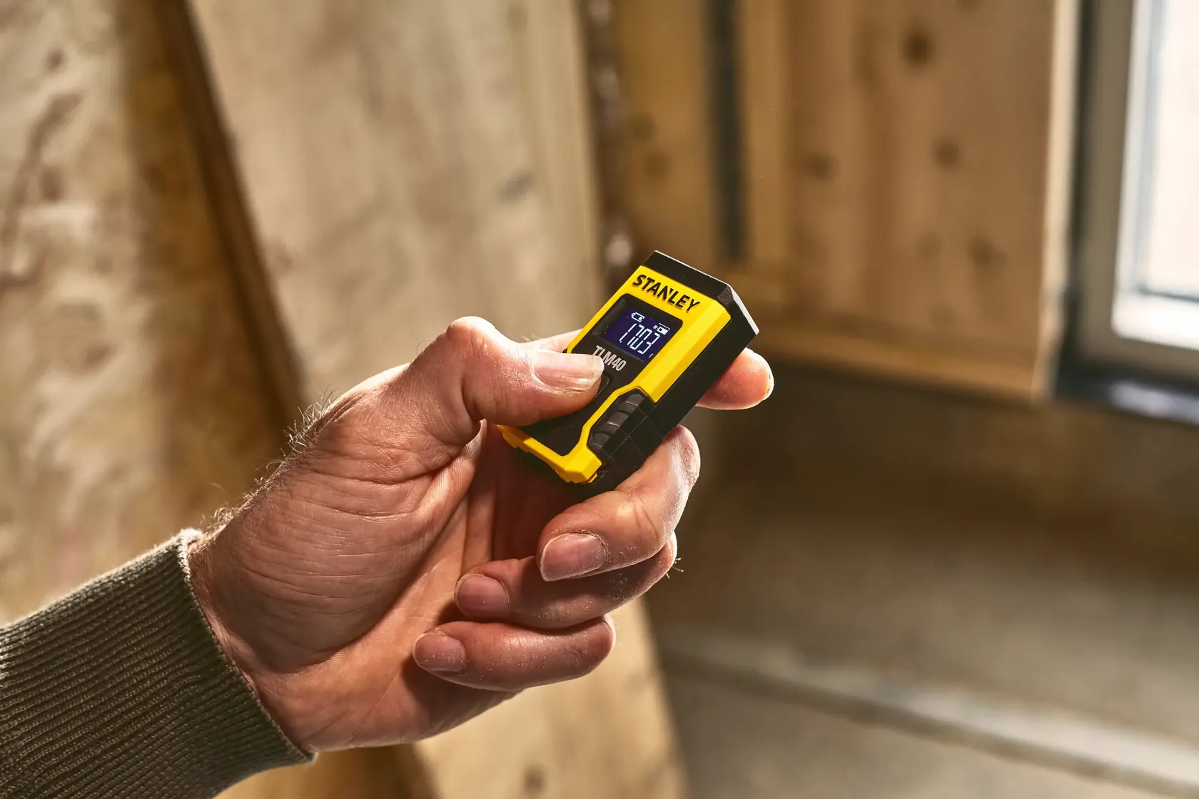 STANLEY STHT77666-0 compact yellow and black laser distance measurer in hand, indoor setting.