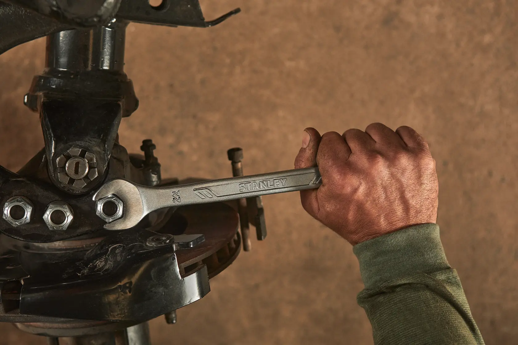 STANLEY STMT72819 wrench used by a hand to tighten a bolt on mechanical equipment, close-up in workshop.