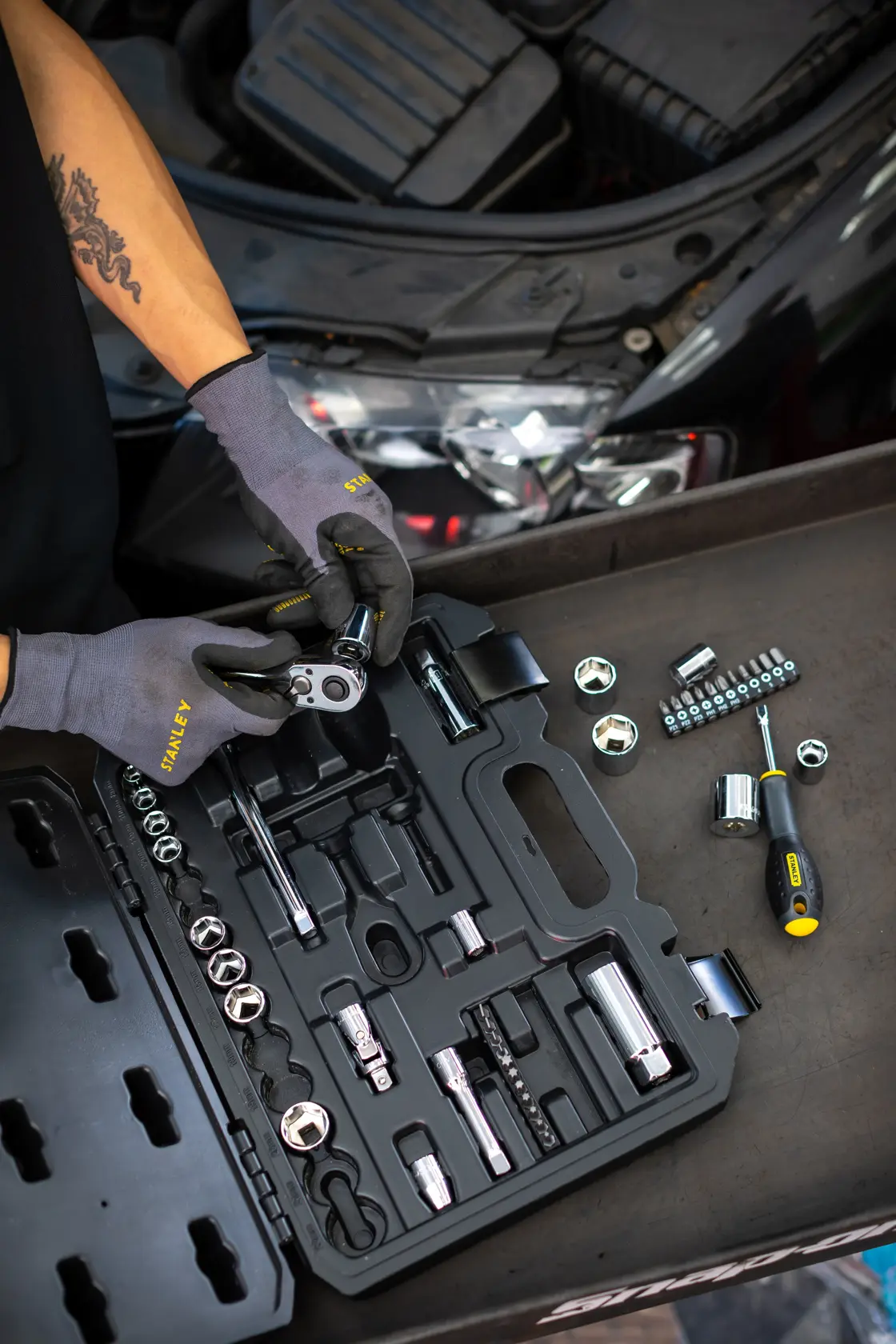 STANLEY STMT82829-1 socket set with ratchet and screwdriver, displayed open by mechanic near car engine.
