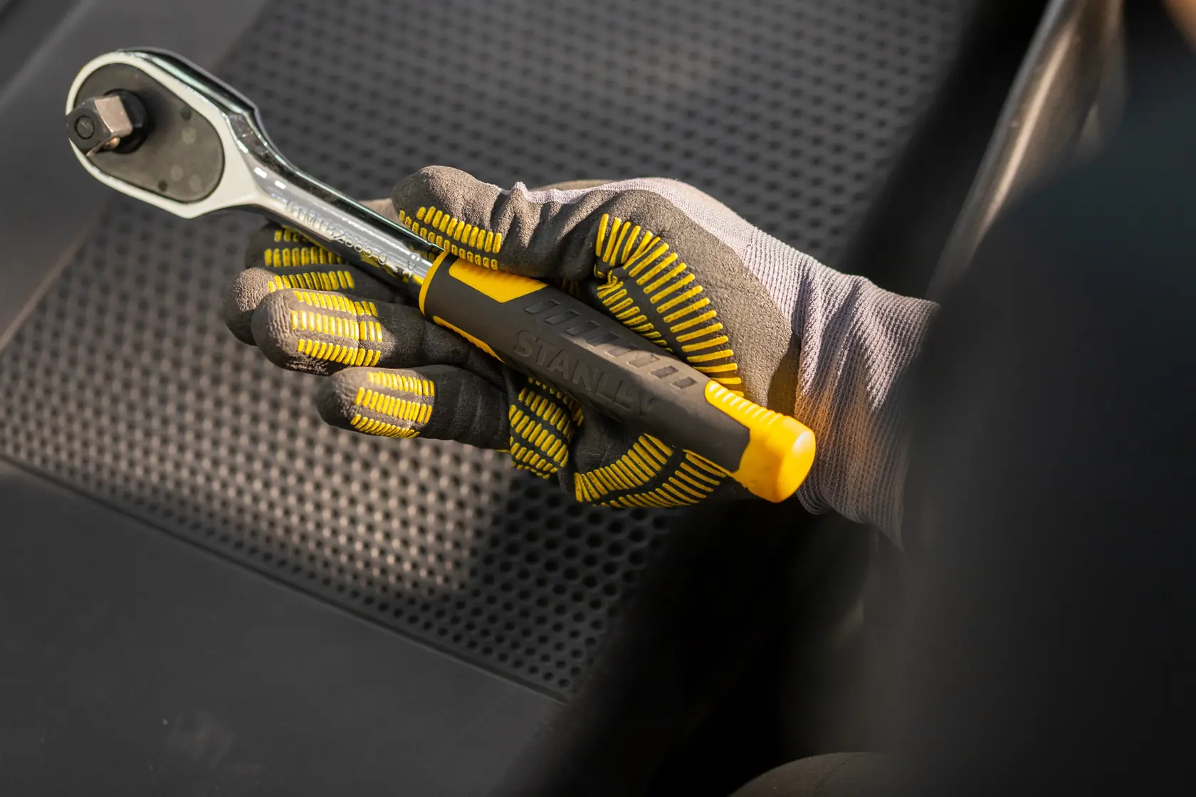 STANLEY STMT82832-1 ratchet wrench with yellow handle held by gloved hand on black car seat.