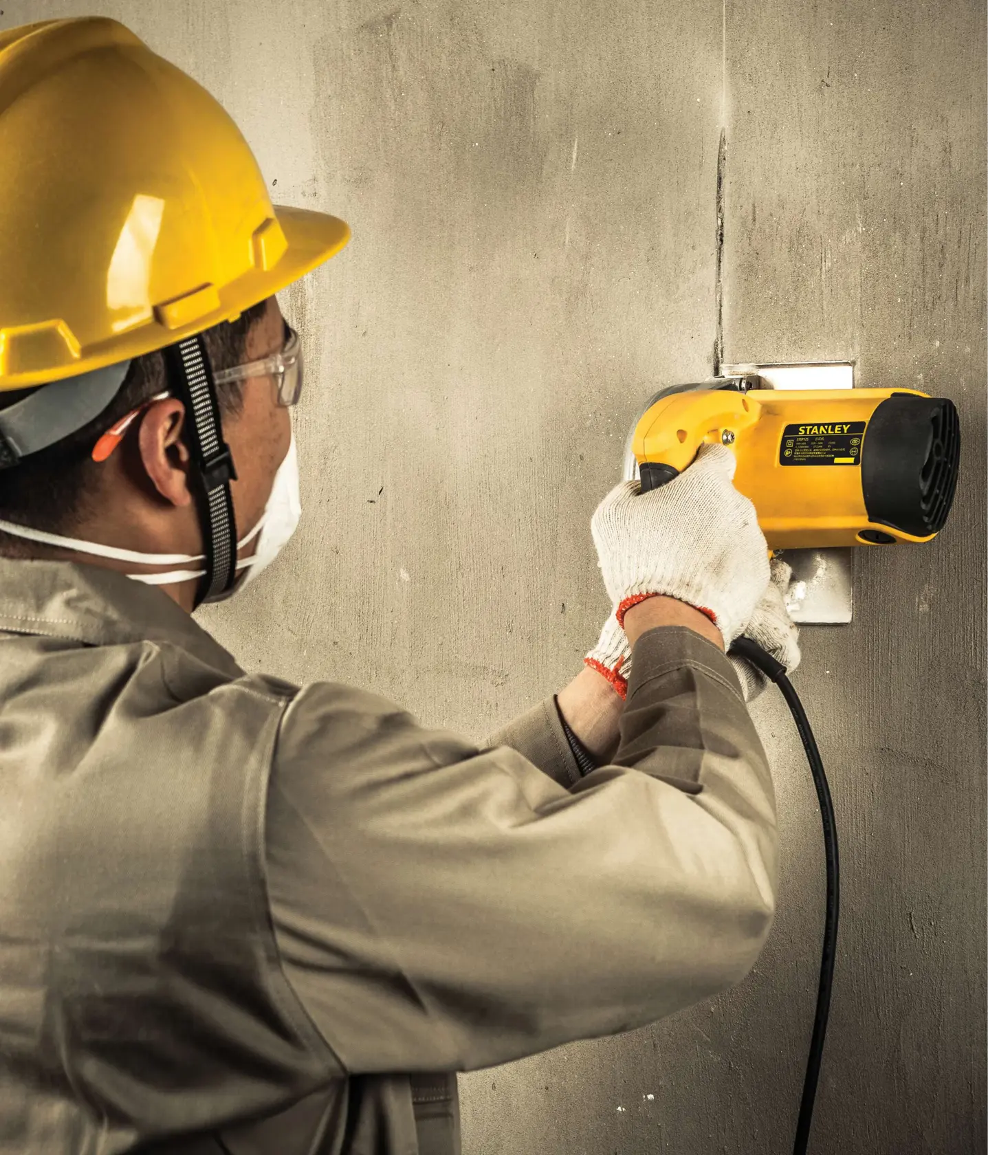 STANLEY STSP125-KR angle grinder in use cutting wall, shown from side, yellow casing, held by worker.
