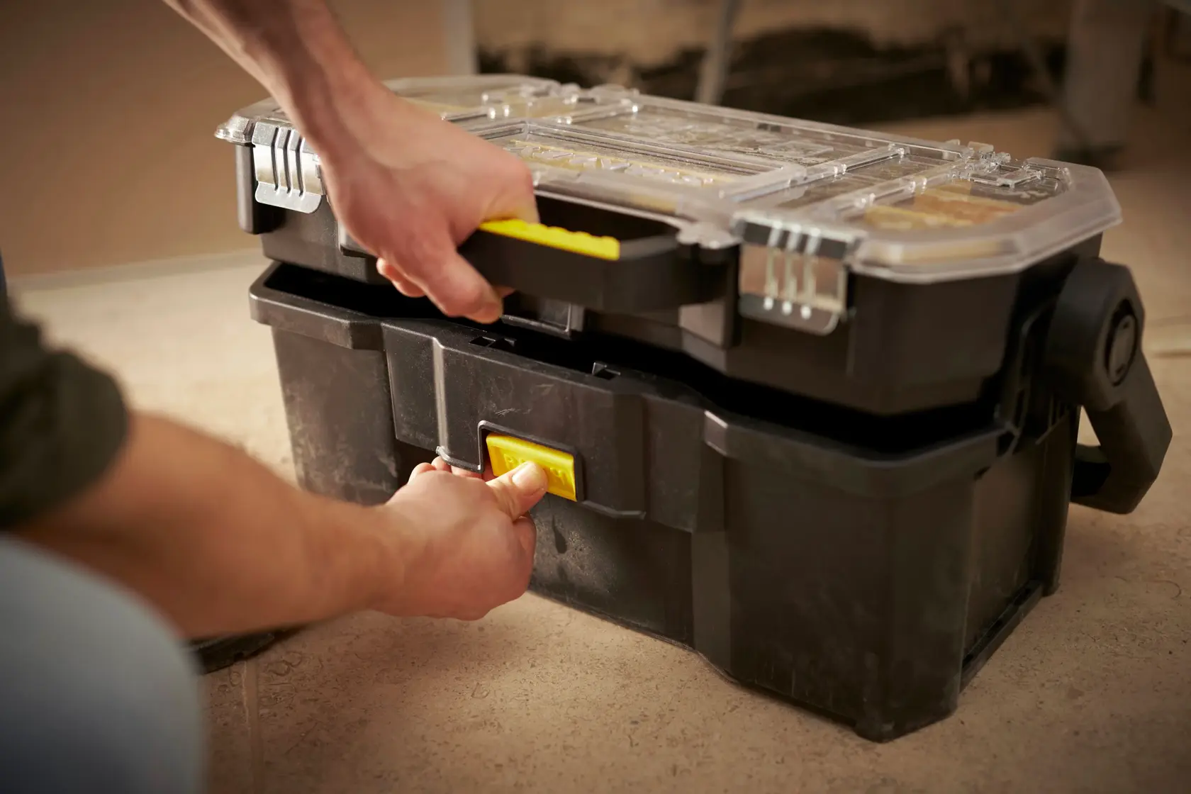 STANLEY STST1-70317 black toolbox with clear lid and yellow handle, shown being opened by hand.