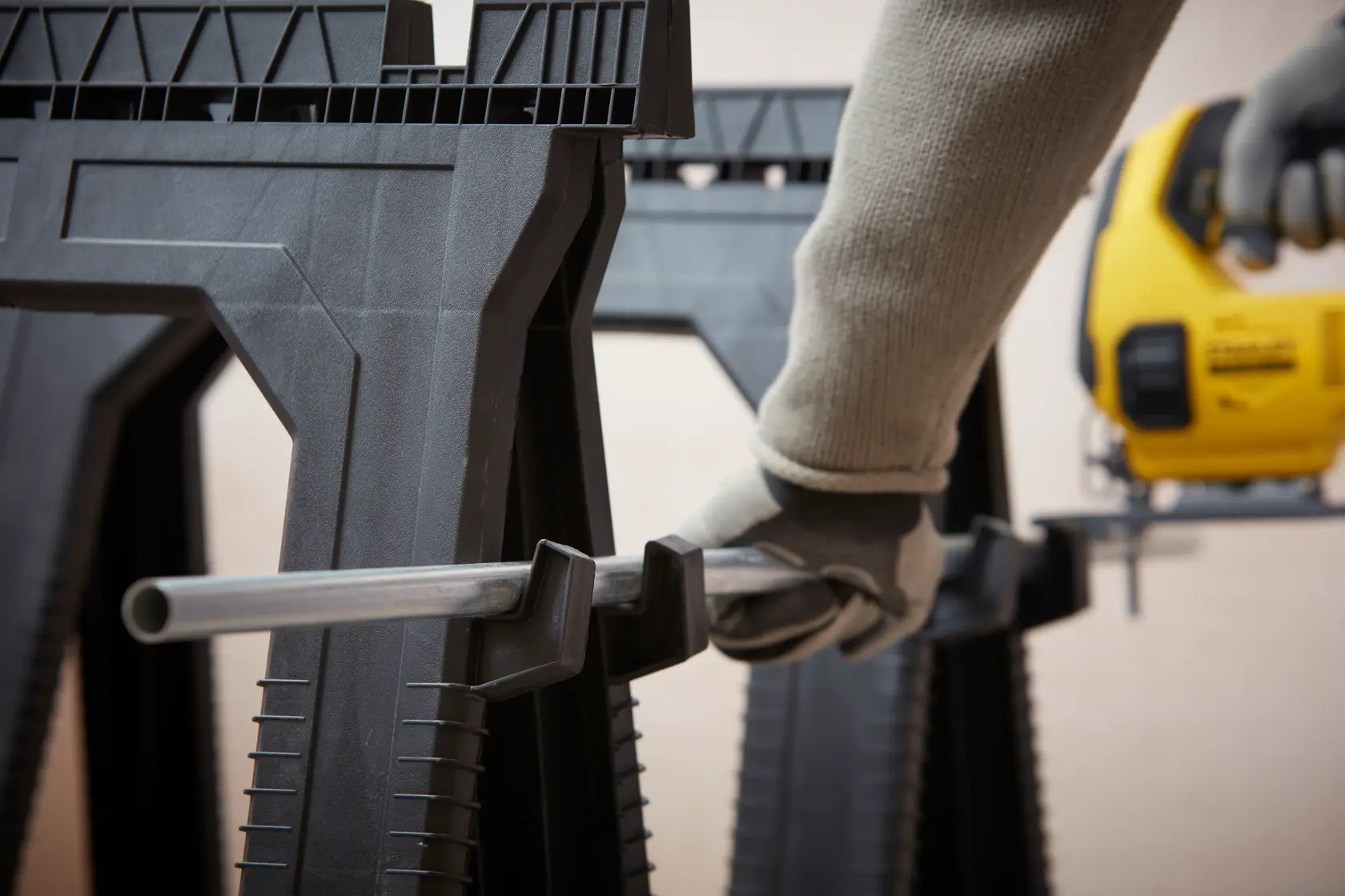 STANLEY STST1-70713 saw horse close-up with glove hand holding metal pipe, DEWALT jigsaw in background.