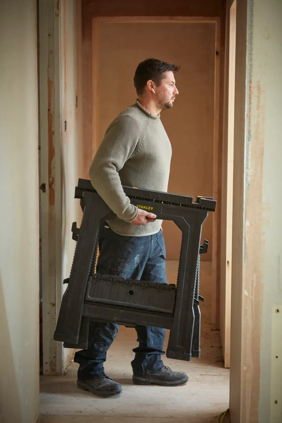 Photo of a person carrying a folded STANLEY STST1-70713 sawhorse in a construction setting.