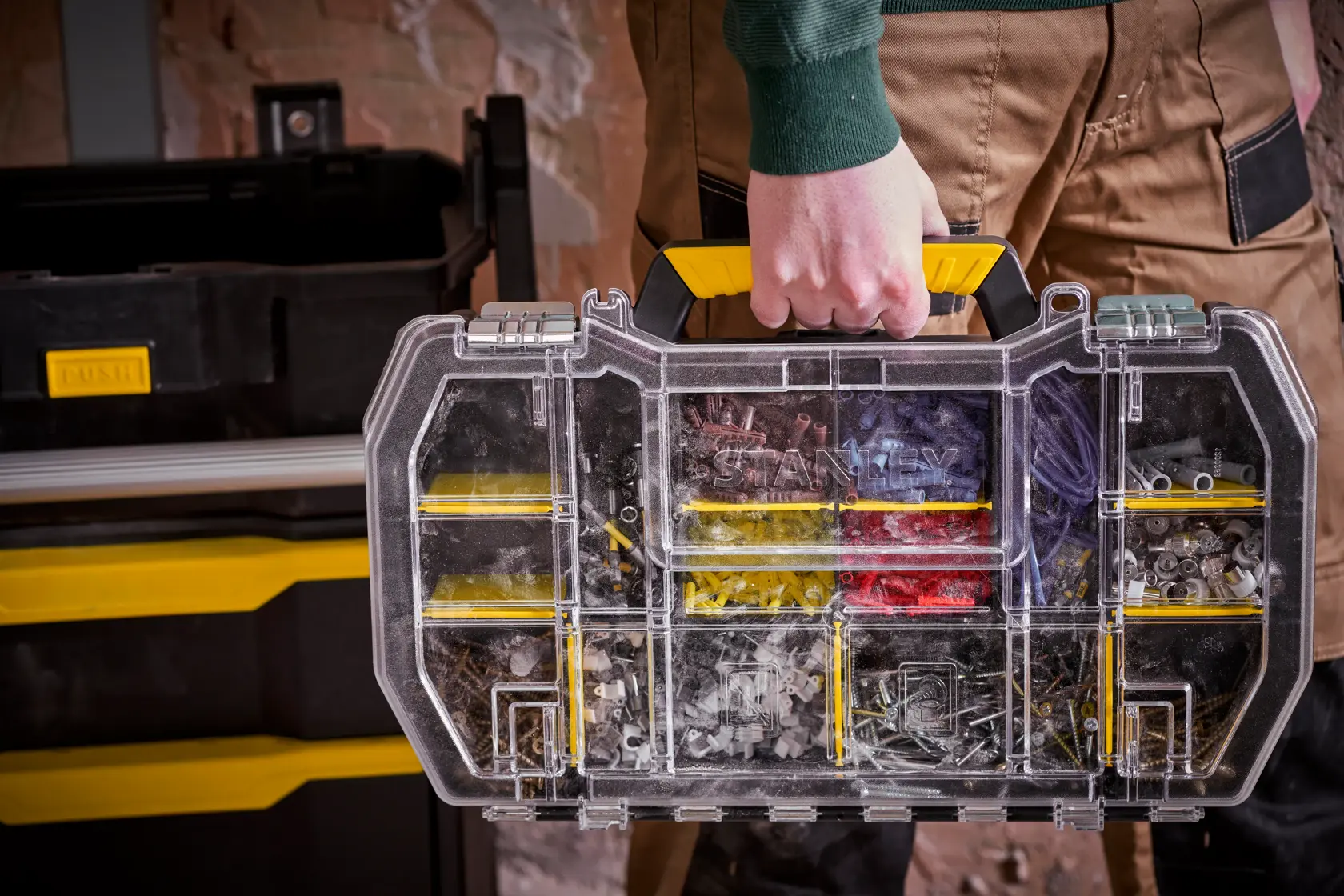 STANLEY STST1-79231 organiser with yellow handle, clear lid, assorted hardware compartments, carried by hand.
