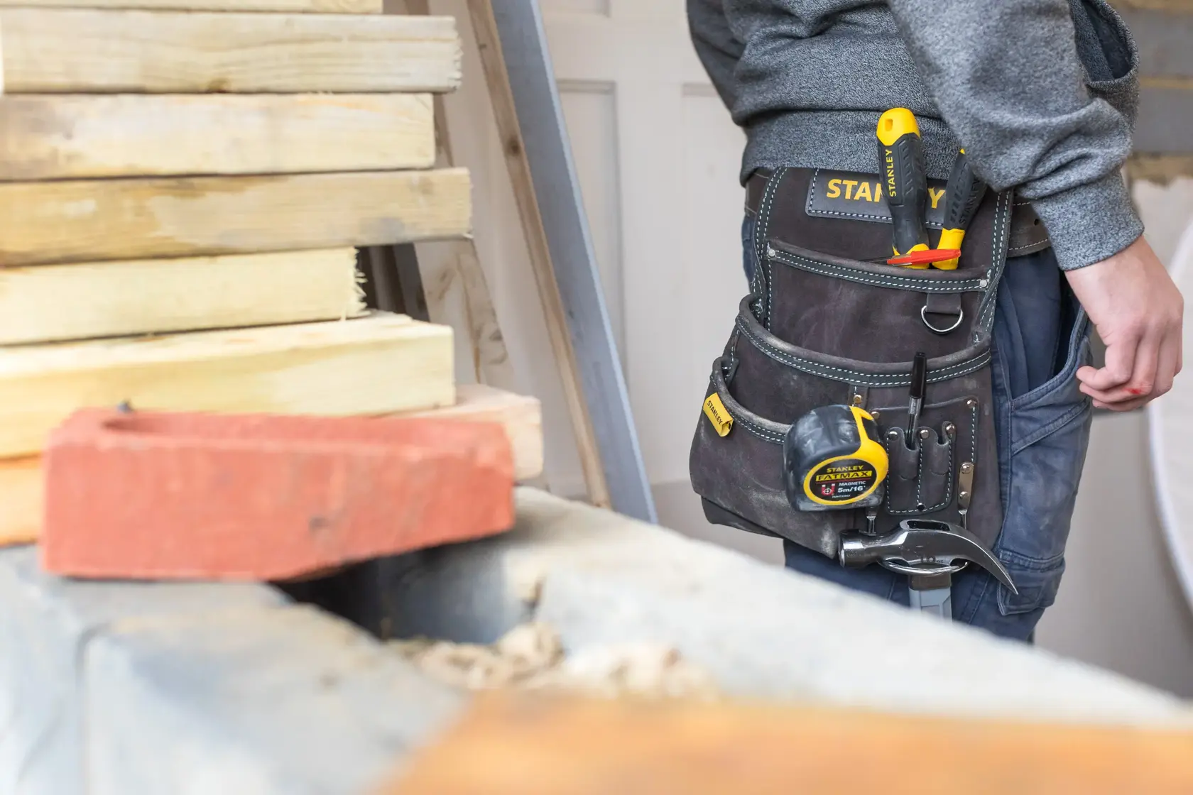 Photo of STANLEY STST1-80114 tool belt with yellow tape measure and hand tools worn by a person at a worksite.
