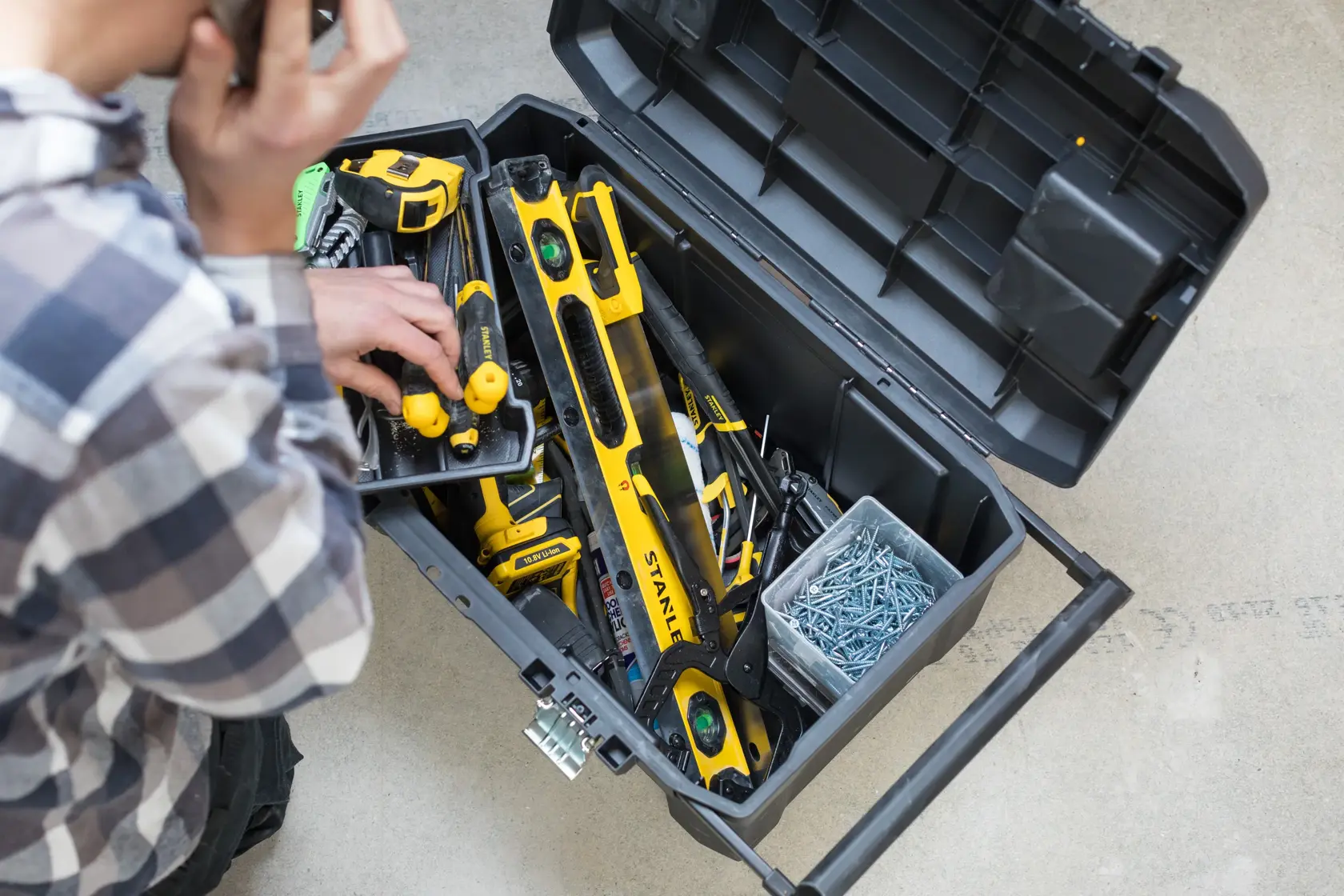 STANLEY STST1-80150 toolbox open, top view with assorted yellow tools and screws inside, user hand visible.