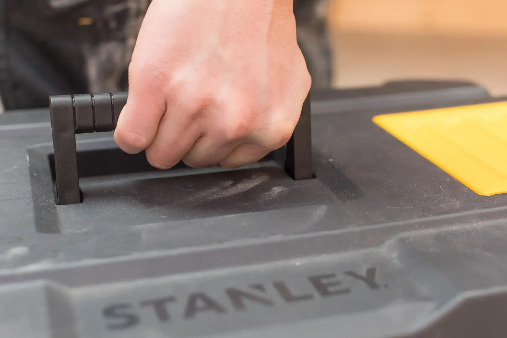 STANLEY STST1-80150 toolbox handle close-up with hand gripping, black and yellow plastic.