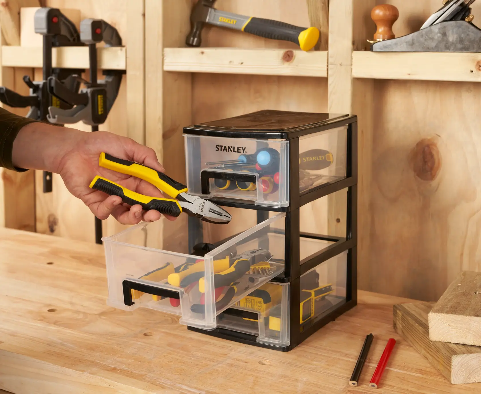 STANLEY STST40711-1 three-drawer tool organizer, photo in workshop setting with hand holding pliers.